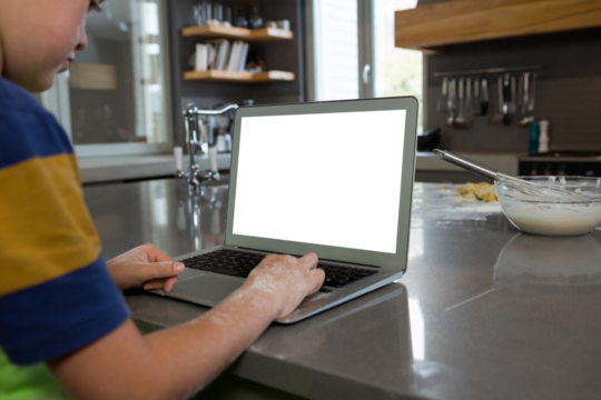 Boy using laptop in kitchen - Powered by Adobe