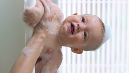 Cute healthy six month old baby bathing with foam and soap bubbles. Vertical video. - Powered by Adobe