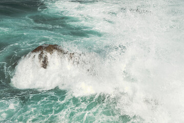 huge crash as salty wind swept ocean waves smack against coastal rocks creating sea foam on the waters surface