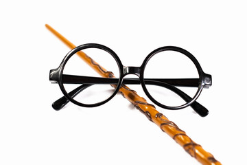Round black eyeglasses and brown magic wand isolated on white background. Harry Potter style circle glasses and wand. Wizard costume accessories.  - obrazy, fototapety, plakaty