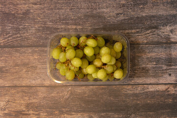 plastic packaging with a bunch of green grapes on an old wooden table with space for text