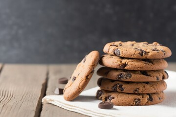chocolate chip cookies, stack of chocolate chip cookies on a wooden table, chocolate chip cookies on top of white dish towel on a white wooden table