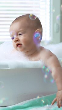 Cute healthy six month old baby bathing with foam and soap bubbles. Vertical video.