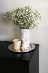 Upper view of a vase with gypsophila flowers on a table with easter ceramic bunny and a candle. 
