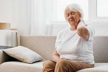 Elderly woman severe neck pain sitting on the sofa, health problems in old age, poor quality of life.