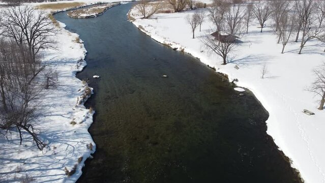Aerial shot of a clear river flowing downstream in a park in winter