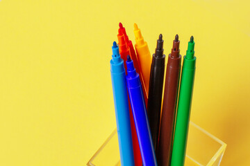 Felt-tip pens without caps of different colors on a yellow background.