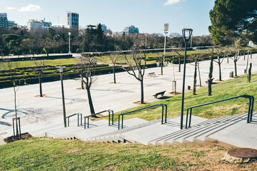 Wide-angle shot captures the grandeur of Parque Eduardo VII, from the top of a staircase, showcasing the vast expanse of green grass, benches, and a wide walkway, inviting visitors to explore the park