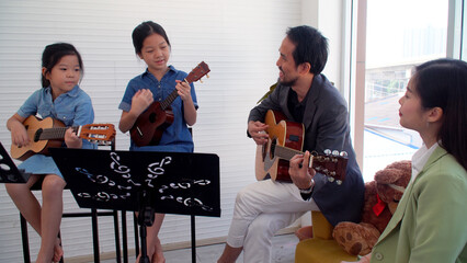 Activity two asian little girl leaning play ukulele together teacher in classroom. Cheerful daughter study playing acoustic guitar music relax information indoors. Lifestyle hobby musical education.