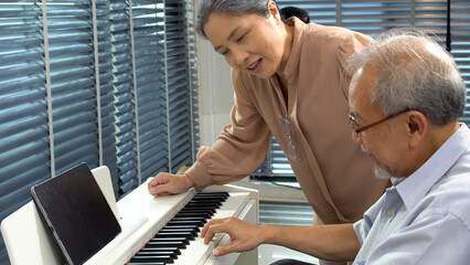 Cheerful active asian elderly man playing keyboard piano musician enjoy at home. Retired senior...