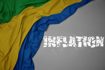 waving colorful national flag of gabon on a gray background with broken text inflation. 3d...