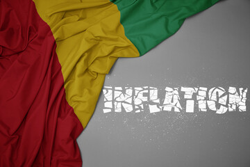 waving colorful national flag of guinea on a gray background with broken text inflation. 3d illustration