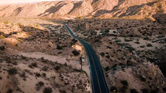 Aerial drone footage of a single white vehicle car driving on the road to Pioneertown, California. 