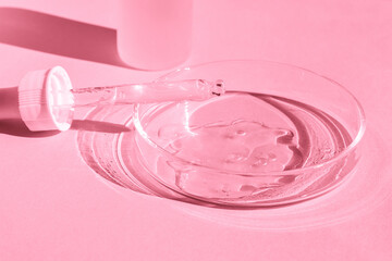 Petri dish. With transparent gel. With a pipette. Cosmetics bottle. On a pink background.