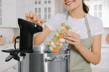 Woman putting vacuum packed vegetables into pot and using thermal immersion circulator in kitchen,...