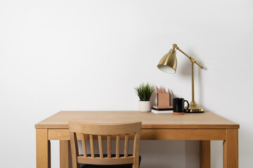 Comfortable workplace with wooden desk near white wall at home