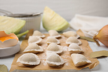 Raw dumplings (varenyky) with tasty filling and flour on parchment paper, closeup