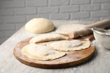 Raw chebureki with tasty filling and rolling pin on wooden table