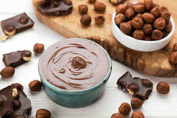 Bowl with tasty paste, chocolate pieces and nuts on white wooden table