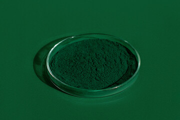 Fresh spirulina algae powder on a green background, in a petri dish, on a green background, organic spirulina powder