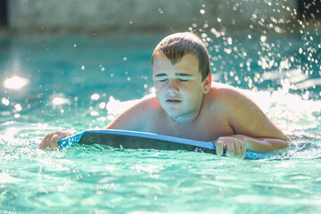 Adolescent boy swimming on boogie board in backyard pool in the summer