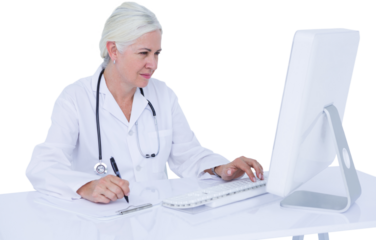Female doctor using computer while writing on clipboard at desk