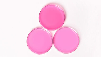 Three Petri dishes with pink liquid. On a white, light background. View from above.