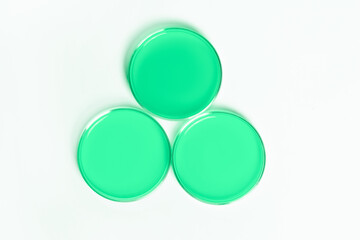 Three Petri dishes with green liquid. On a white, light background. View from above.