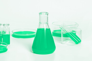 Flask for a laboratory with a green liquid. Against the background of laboratory glassware. Petri dishes, flasks, test tubes. On a white, light background.