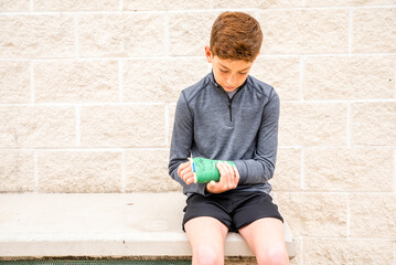 Young preteen boy athlete with cast sitting on bench outside © 3Days2Go Media