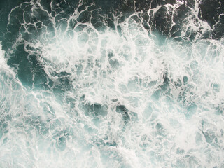 white sea foam on the ocean surface is agitated salt water from crashing waves and a strong surf,...