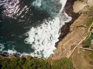 large rogue wave slams onto rocky shore which churns and oxygenates the blueish green sea foam and...