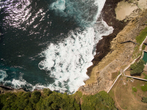 large rogue wave slams onto rocky shore which churns and oxygenates the blueish green sea foam and sprays a salty mist into the air, the ocean waters turns clear as the undertow current pulls back