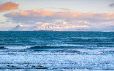 Snowy Mountains at Winter, Sunrise with Fluffy Clouds and Stormy Sea in Iceland. Landscape in North Europe Country. Atlantic Ocean Coast and Icelandic Fjords.