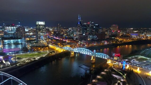 Aerial Shot Of Famous Bridges On Cumberland River In City, Drone Flying Backwards During Illuminated Night - Nashville, Tennessee