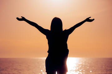 Silhouette of a Woman With her Arms Outstretched in Sunset View. Carefree girl feeling excitement and positivity  
