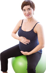 Smiling pregnant woman holding belly while sitting on erercise ball