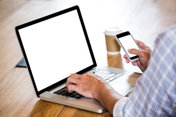 Human hands holding mobile and working on laptop