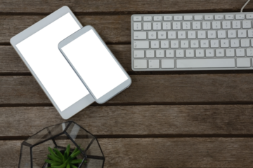 Digital tablet, mobile phone, pot plant and keyboard on wooden plank