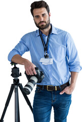 Portrait of serious young photographer holding camera while leaning on tripod