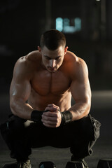 Fototapeta premium Sportsman with well trained body sitting with dumbbells on the floor in fitness gym