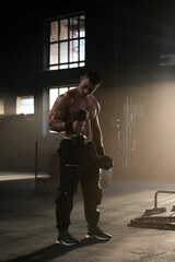 Full shot of a strong athletic sweaty man doing shirtless workout at gym, training with dumbbells