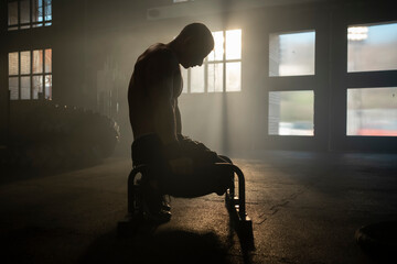 Man with muscular body doing calisthenics training on parallettes bar on floor at gym