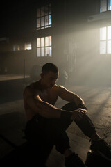 Sportsman with well trained body sitting on the floor in fitness gym