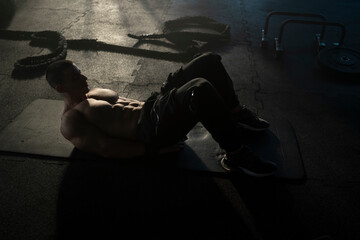 Young muscular sportsman lying on the floor mat doing abs isolation workout in an indoor workout area