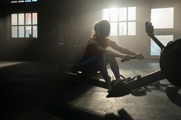 Young fitness woman working out on rowing machine in gym. Female athlete training at exerciser in...