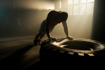 Athletic young man performing push ups on tyre, exercising at warehouse enjoying physical activity
