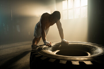 Young shirtless boxer man pushing ups on a big tire in training session at the gym