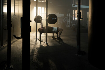 Male bodybuilder lying down on gym bench and pressing a large barbell upwards