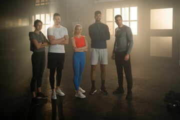 Fototapeta premium A group of young men and women standing in gym, posing at camera, looking strong and confident